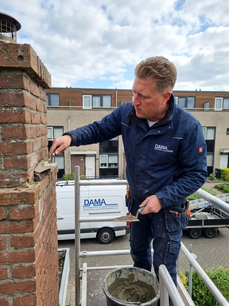 Vakman van Dama Schoorsteen- en Geveltechniek herstelt voegen van een gemetselde schoorsteen vanaf een steiger